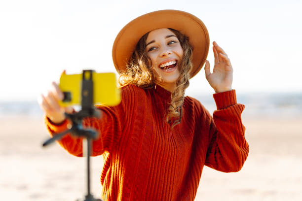 istock Young woman using smartphone with stabiliser  to create video content for social media on a sunny beach. 2200127463