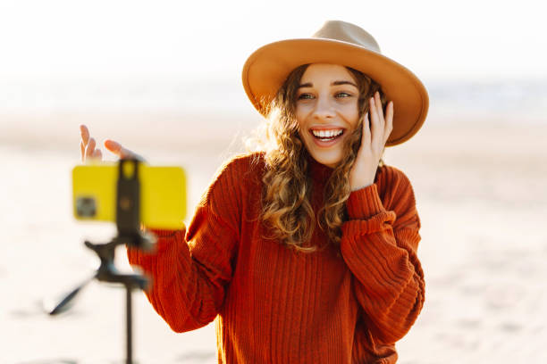 istock Young woman using smartphone with stabiliser  to create video content for social media on a sunny beach. 2200127490