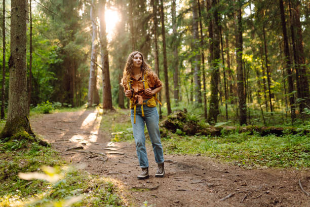 istock Young woman carrying backpack while walking among trees in the forest. 2200128551