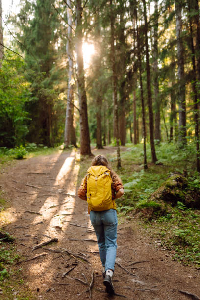 istock Young woman carrying backpack while walking among trees in the forest. 2200128575