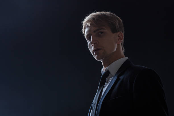 istock In a dark studio, a man in a black suit and white shirt stands in profile. 2200128641