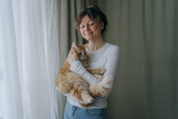 istock Woman holding ginger cat near window with curtains 2200128724