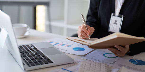 istock Financial professional taking notes and analyzing data on a laptop at a modern office desk. 2200129343