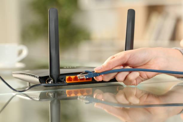 istock Woman hand plugging network cable to a modem at home 2200130560
