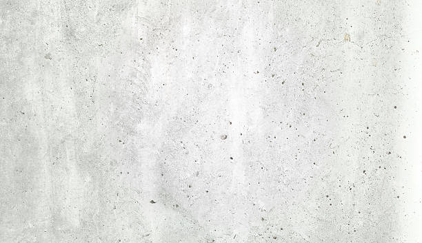 istock Large white grunge textured concrete wall background. The backdrop is a rough cement floor in gray tones. 2200132438