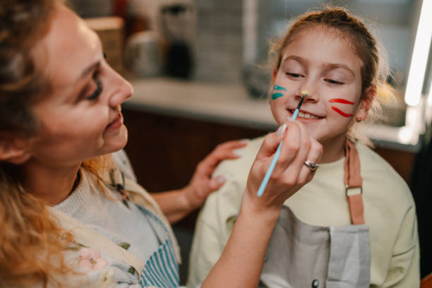 istock Mother painting daughter's face with colorful stripes in kitchen 2200132941