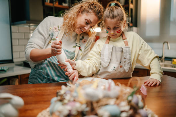 istock Mother and daughter decorating easter cookies together in kitchen 2200132994