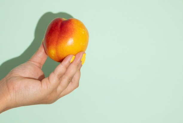 istock Female hand holding a peach on a light green background with copy space 2200133237