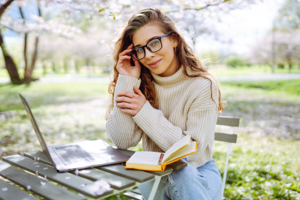istock Young woman sitting on blooming park and using laptop. 2200134881