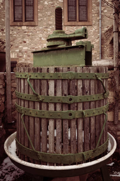 An elegant vintage fruit press is situated in a historic stone courtyard, evoking the charm of traditional winemaking practices and surrounded by aged architecture.
