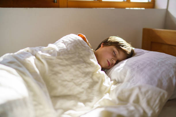 A boy sleeps in bed during a sunny morning in his bedroom