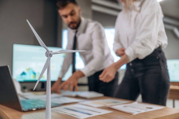 istock Blurred, focused on wind turbine model. Two employees are working in company 2200146483