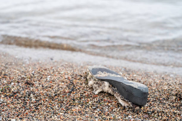 istock Old shoe sole washed ashore on beach, waves in background, ocean pollution 2200148019