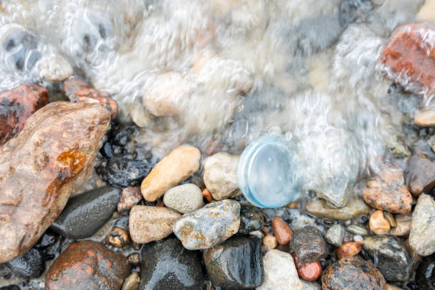 Wave washes over plastic cap on pebble beach, emphasizing ocean pollution problem in close-up
