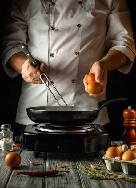 istock A skilled chef prepares to crack fresh eggs into a sizzling skillet, surrounded by ingredients and kitchen tools. The warm lighting and rustic setting enhance the culinary ambiance 2200149922