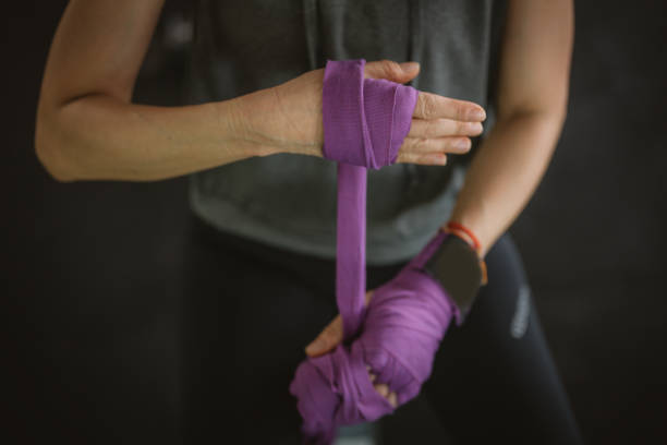 An Asian female kickboxer is wrapping her hands with bandages at a health club gym.