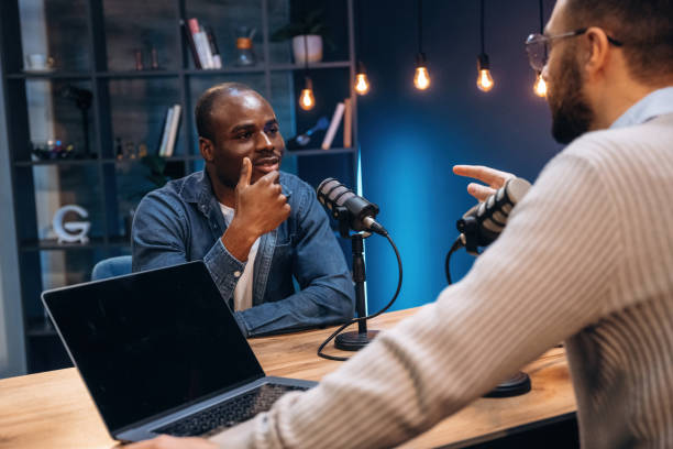istock Sitting by the table. Two radio presenters recording an audio broadcast in a studio 2200155363