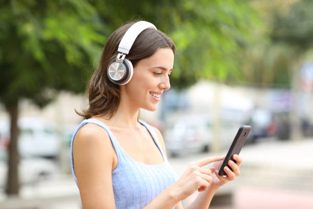 istock Happy woman using phone and headphone in a park 2200160434