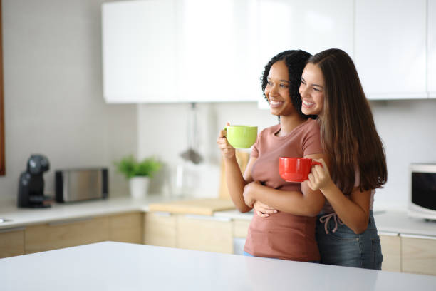 istock Lesbian interracial couple drinking in a kitchen looking away 2200160463