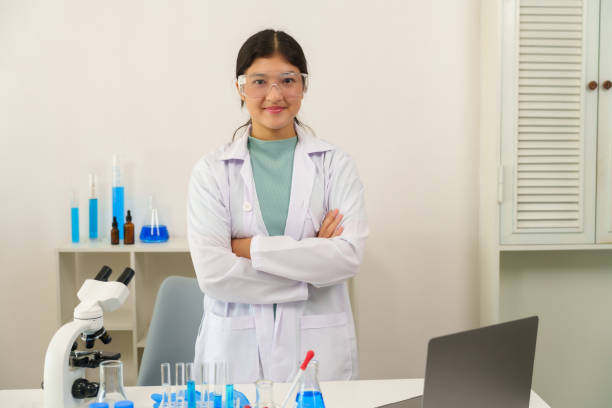 istock Caucasian school children learning experiment in science classroom. Young female student wearing lab coat and safety goggles standing confidently with arms crossed in modern laboratory. 2200168053