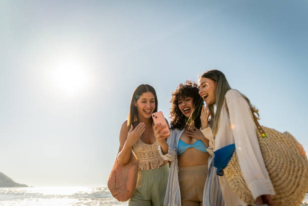 Young friends women using mobile phone on the beach