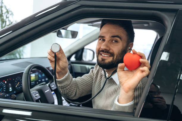 Stethoscope and red little heart model. Man is with the car in dealership stock photo