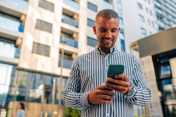 istock Young manager smiling and texting on phone in front of office building 2200182458