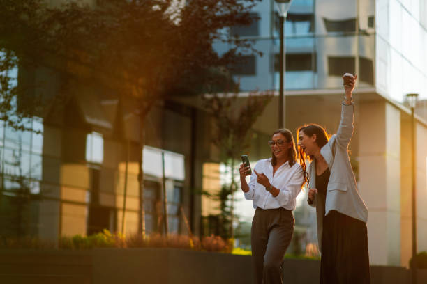 istock Two young businesswomen celebrating success outdoors while looking at smartphone 2200182549