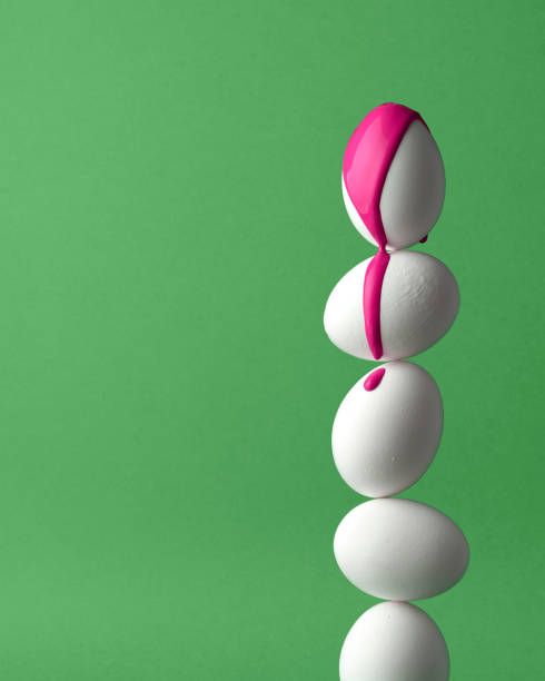A stack of white eggs on a green background, with the top egg covered in bright pink paint dripping down. Easter concept, a symbol of renewal and creativity.
