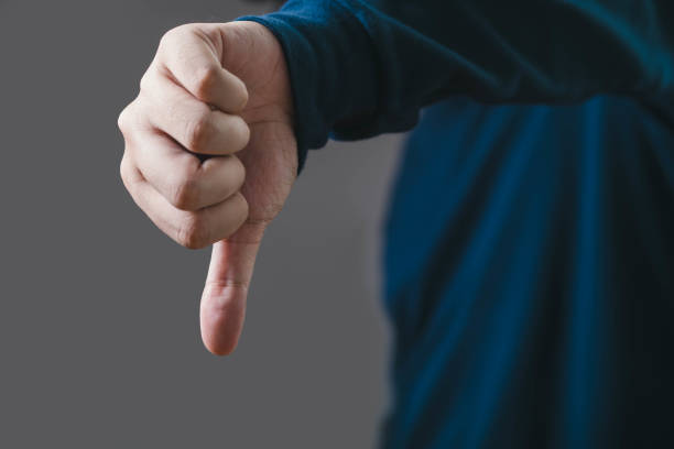 istock A close-up image of a hand displaying a thumbs-down gesture against a neutral background, symbolizing disapproval, rejection, or negative feedback. 2200186255