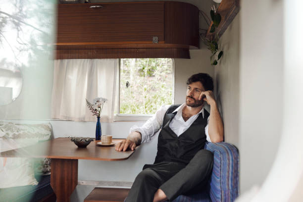 Caravan, man and thinking by window for travel, memory and planning for future with reflection. motor camper, male person and remember in lounge for contemplating, vacation and thoughts for journey