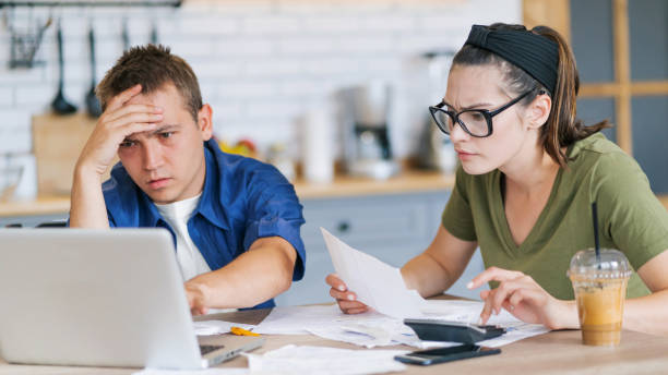 istock Couple calculating bills at home using tablet and calculator. Young couple working on computer while calculating finances sitting on couch. Young man with wife at home analyzing their finance with documents 2200189413