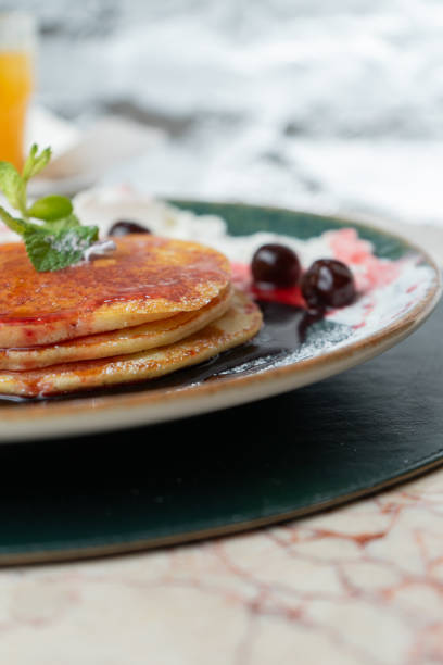 Pancakes with maple syrup, cream and black cherry on a bar table