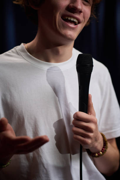 istock Smiling Young Person Holding Microphone on Stage 2200196015