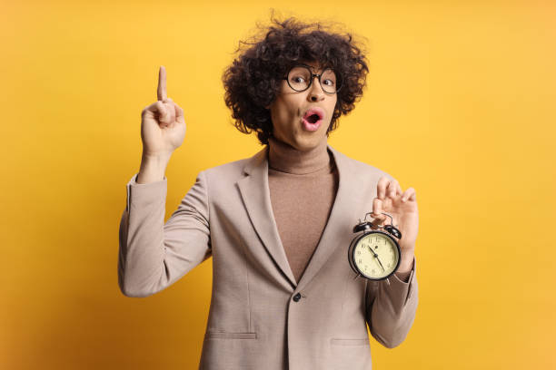 istock Young man holding an alarm clock and pointing 2200209194