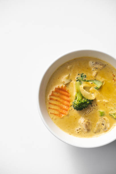 Minimalistic top view of Thai yellow curry with vegetables served in a white ceramic bowl, Creamy coconut-based broth with broccoli, carrots, and mushrooms, Isolated on a white background, Authentic Thai cuisine concept