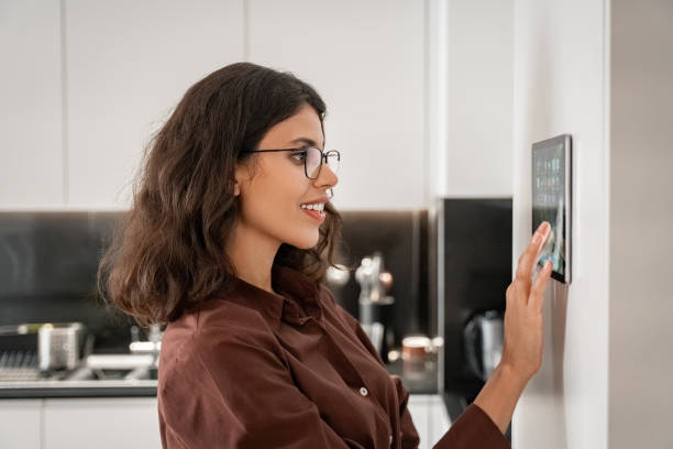 istock Closeup lady enjoy of new intelligence technologies. Smiling young woman using screen device gadget for remote control for air conditioning, cleaning housekeeping, touching tablet computer on wall. 2200209528