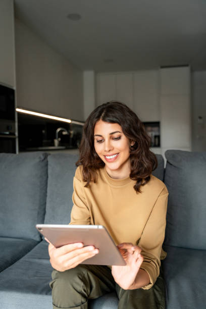 istock Vertical portrait freelance business woman sitting on couch sofa using tablet computer application for work remotely. Latin hispanic girl holding tab gadget, working on digital online project at home 2200209538