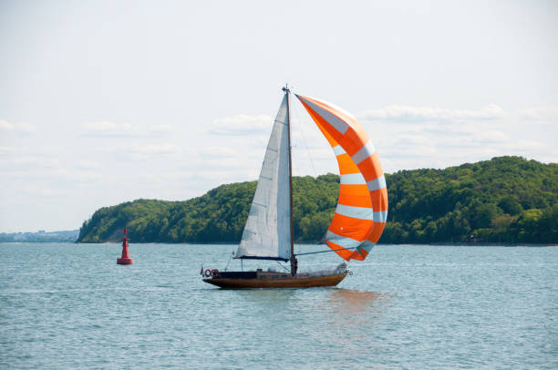 A steady breeze fills the sail of a small pleasure boat as it cruises inside the harbor  breakwall between the port of Cleveland, Ohio and the open waters of Lake Erie 