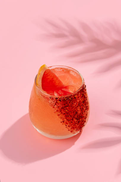 istock Cold and refreshing cocktail with ice garnished grapefruit slice stands on pink background. Summer non-alcoholic cocktail with juice and soda. Hard light, bar menu. 2200210519