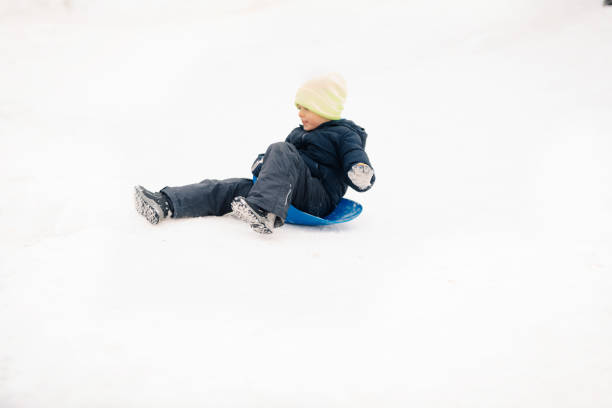 Happy child having fun sliding down a snowy hill on a blue plastic sled, enjoying the winter weather