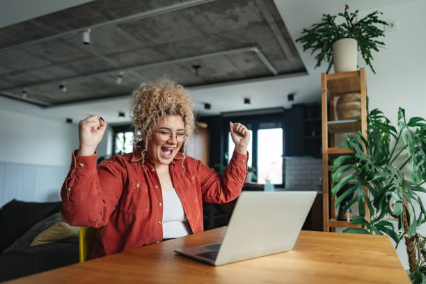excited young woman celebrating success while working from home - 達成 一人 成功 ストックフォトと画像