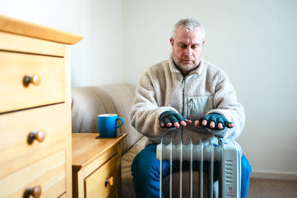 istock Cold worried man warming hands on electric heater at home 2200212982