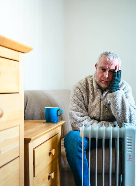 istock Cold worried man warming hands on electric heater at home 2200213017