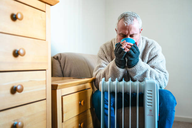 istock Cold worried man warming hands on electric heater at home 2200213100