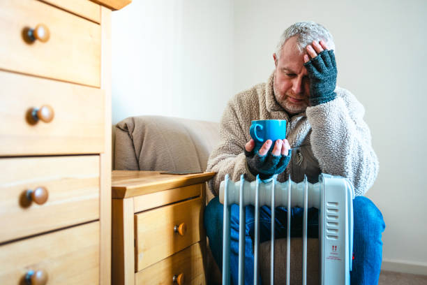 istock Cold worried man warming hands on electric heater at home 2200213106