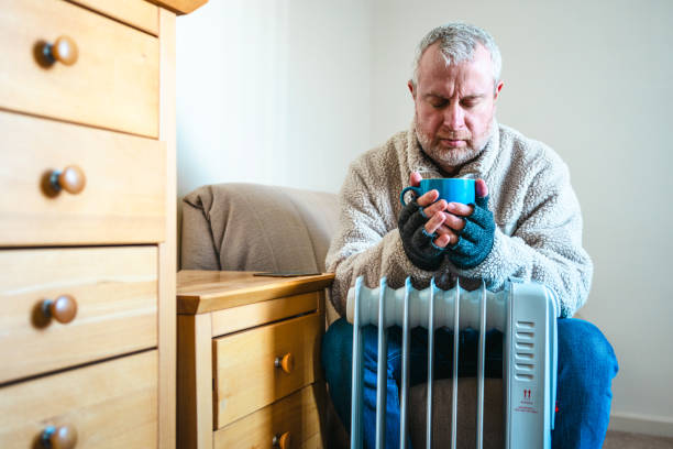 istock Cold worried man warming hands on electric heater at home 2200213111