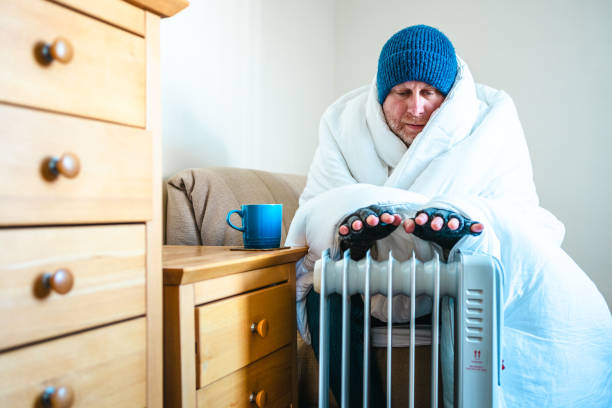 istock Cold worried man warming hands on electric heater at home 2200213179