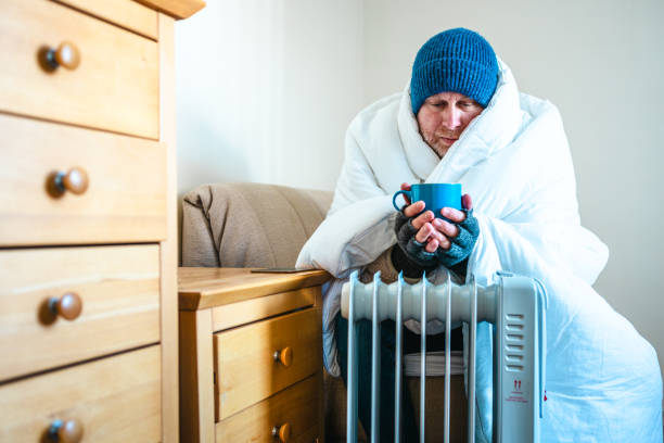 istock Cold worried man warming hands on electric heater at home 2200213180