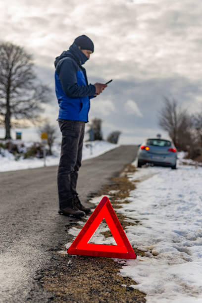 Iturrieta pass. álava province. Spanish basque country. Driver using cellphone next to broken car and warning triangle on a snowy road